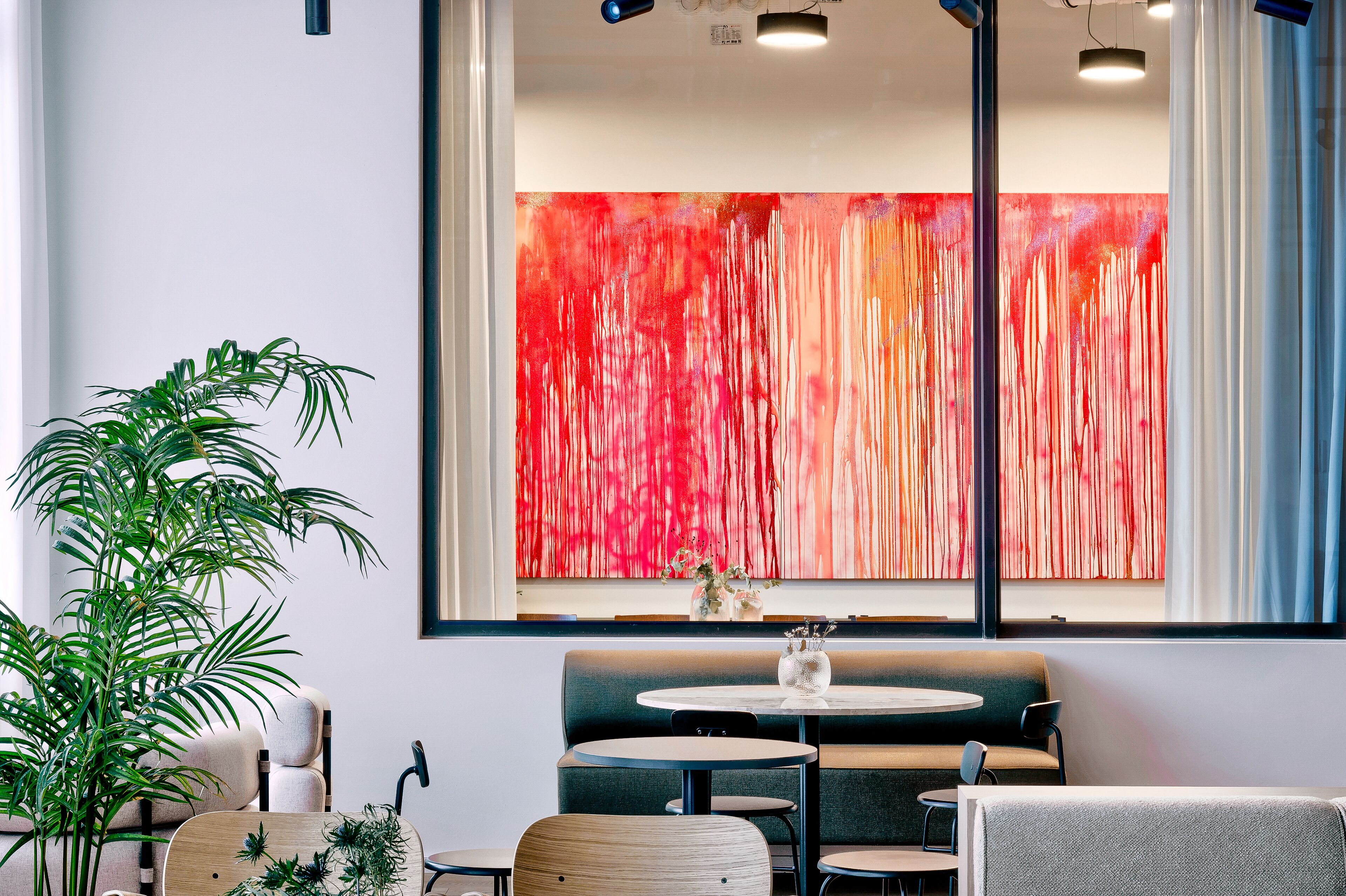 A modern interior with a green sofa, round tables, and a large abstract painting on the wall.