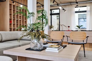 A modern office space with a wooden bookshelf, a sofa, two chairs, a table with a vase of plants, and books.