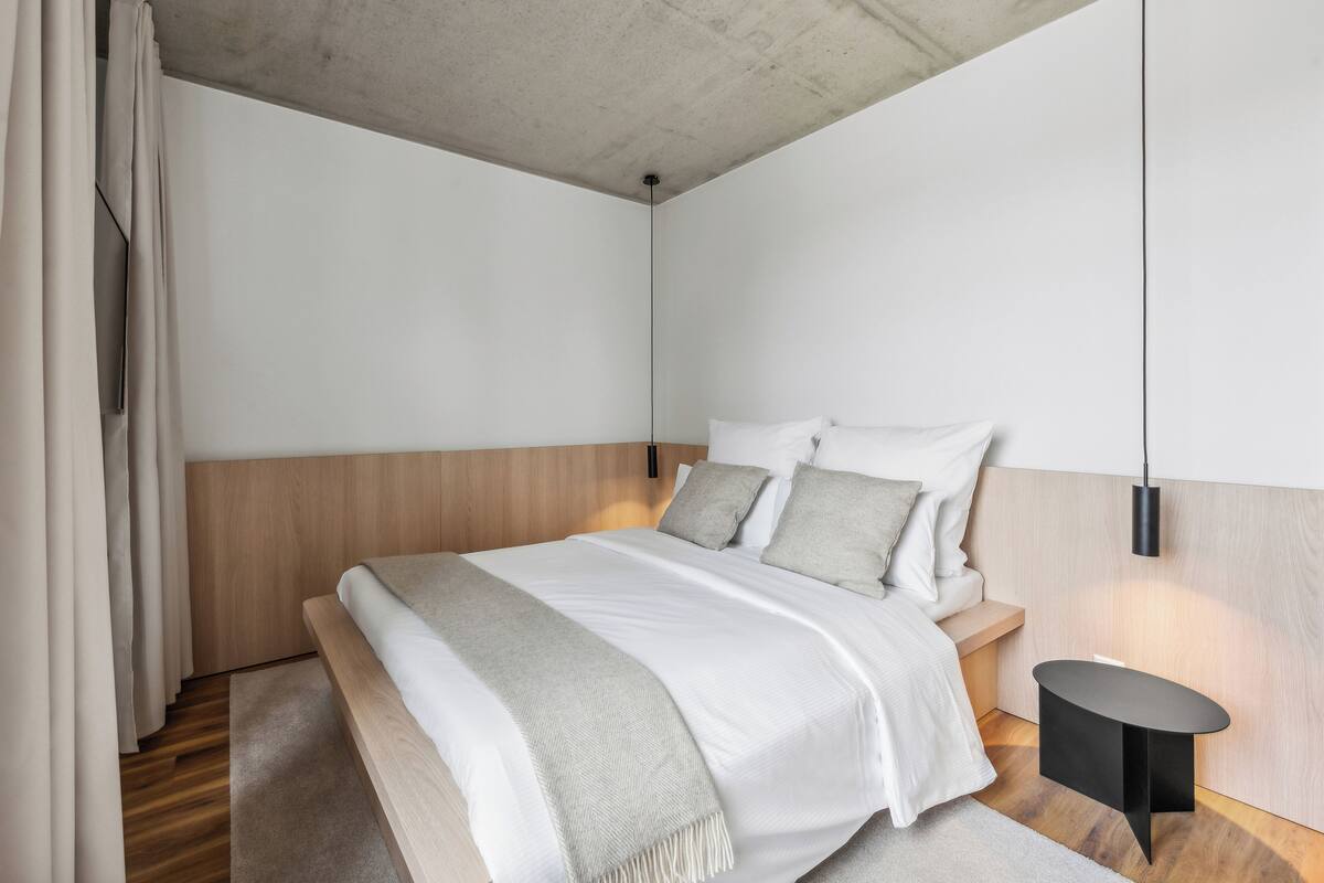 A modern bedroom with a wooden headboard, a bedside table, and a hanging light fixture.