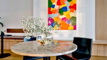 Una mesa redonda con un florero de flores blancas, un cuadro abstracto colorido en la pared y un banco de madera al fondo.