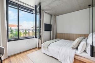 A modern bedroom with a large window, a bed, a TV, and a view of the outside.