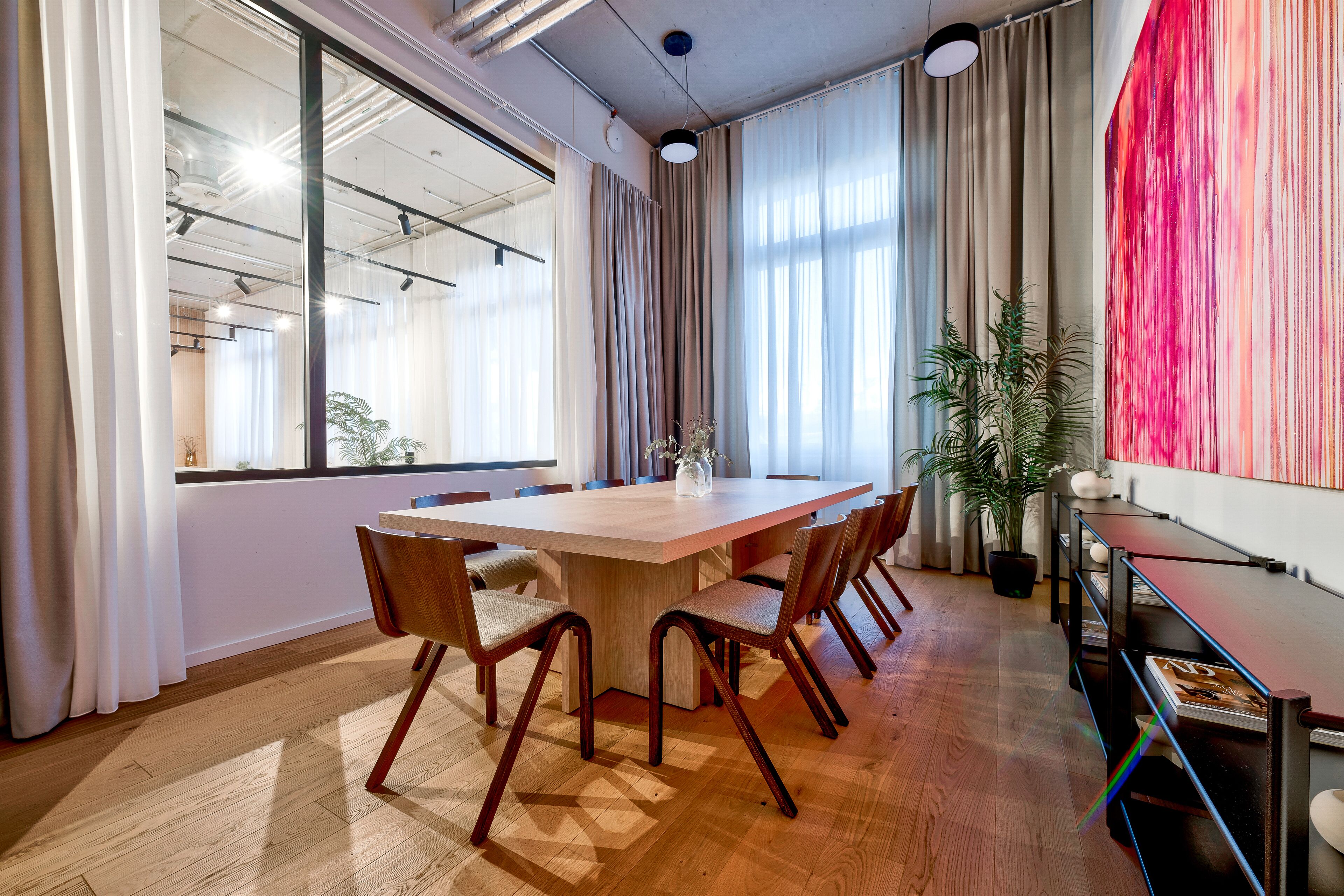 Une salle de conférence avec une grande table en bois, six chaises et une plante en pot.