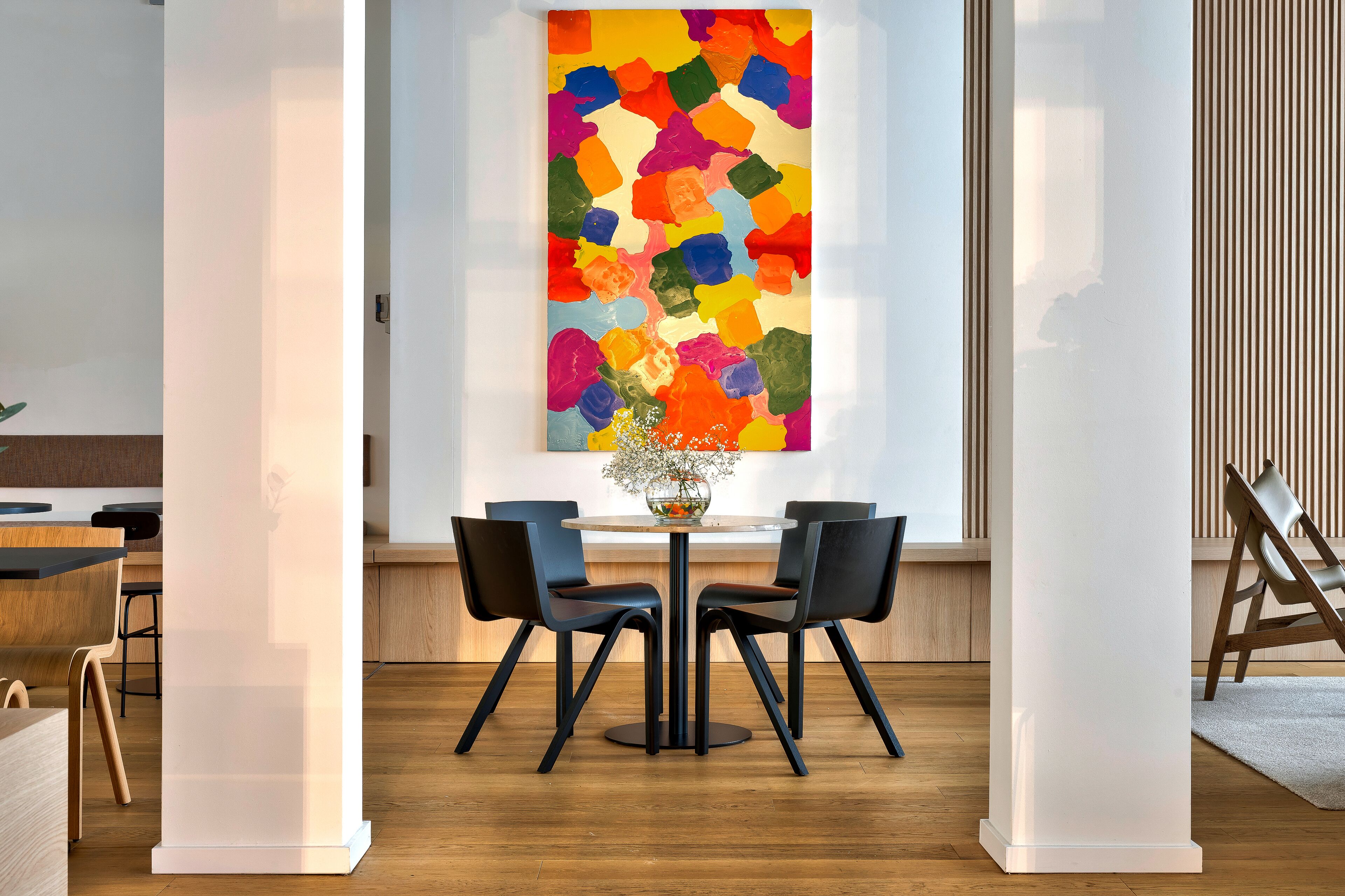 Un comedor moderno con una mesa redonda, sillas negras y un cuadro abstracto y colorido en la pared.