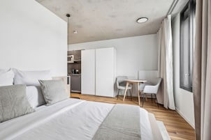A modern hotel room with a large bed, a desk, and a kitchenette.
