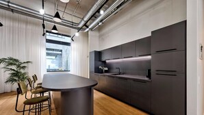 A modern kitchen with dark cabinetry, a central island, and a dining area with chairs. - Habyt Berlin Waterfront (Berlin)