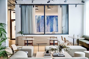 A modern lounge area with a large abstract painting, two round tables, and comfortable seating.