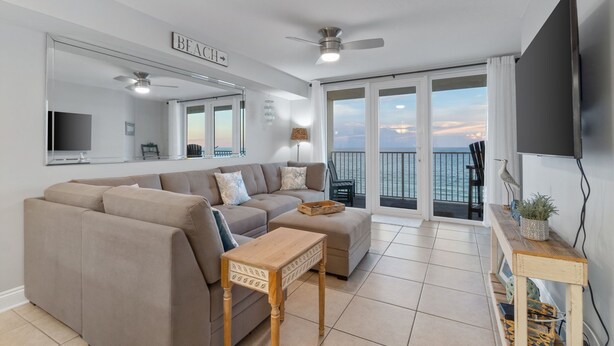Ein modernes Wohnzimmer mit einem beigefarbenen Sofa, einem Holztisch, einem an der Wand montierten Fernseher und einem Balkon mit Meerblick.
