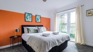 Un dormitorio con cama, mesita de noche, ventana con cortinas y vista a áreas verdes.