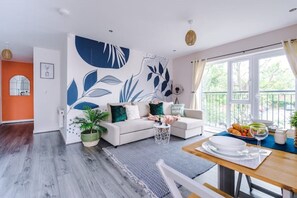 A modern living room with a sofa, a dining table with a plate of food, and a large window with curtains.