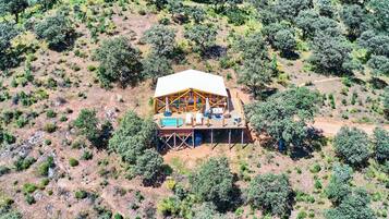 Vue aérienne d’un chalet en bois doté d’une piscine, entouré d’une végétation clairsemée.