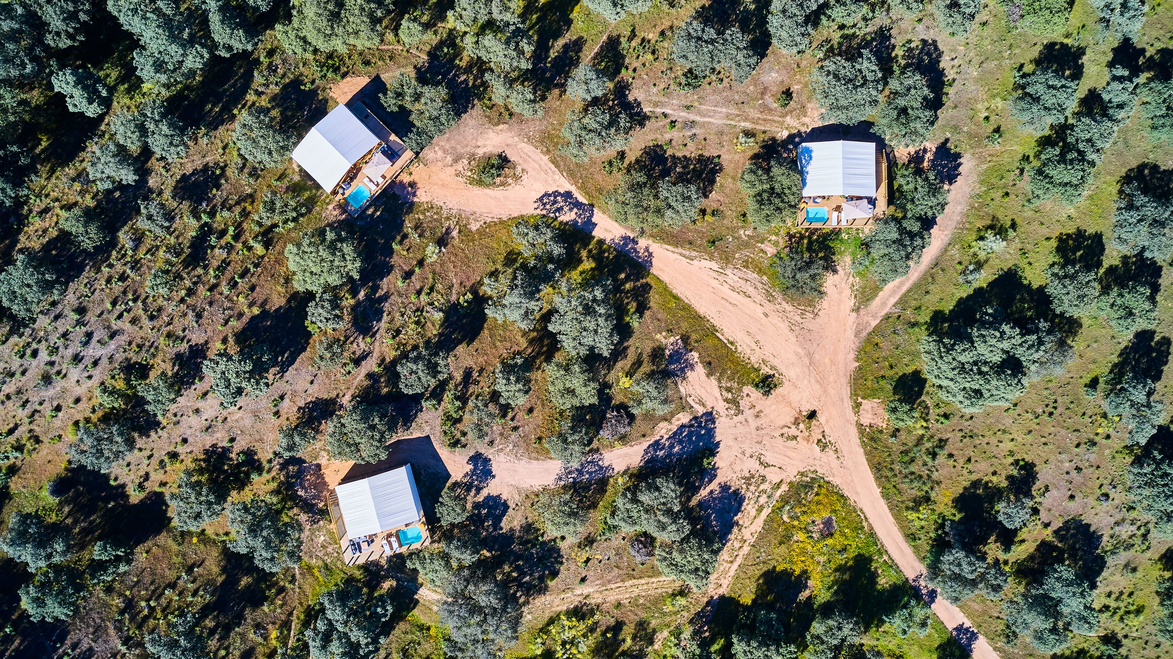An aerial view of a property with three buildings, each with a large roof and a swimming pool.
