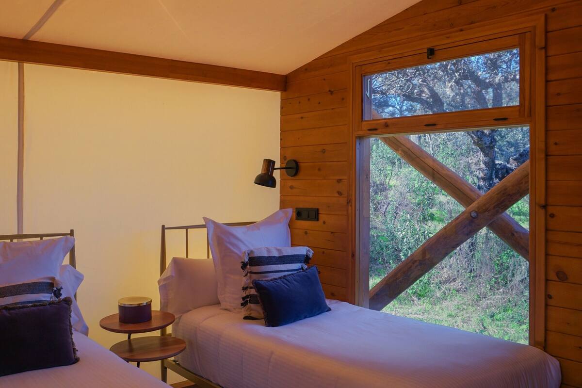 A cabin with two beds, a small table, and a window with a view of trees.