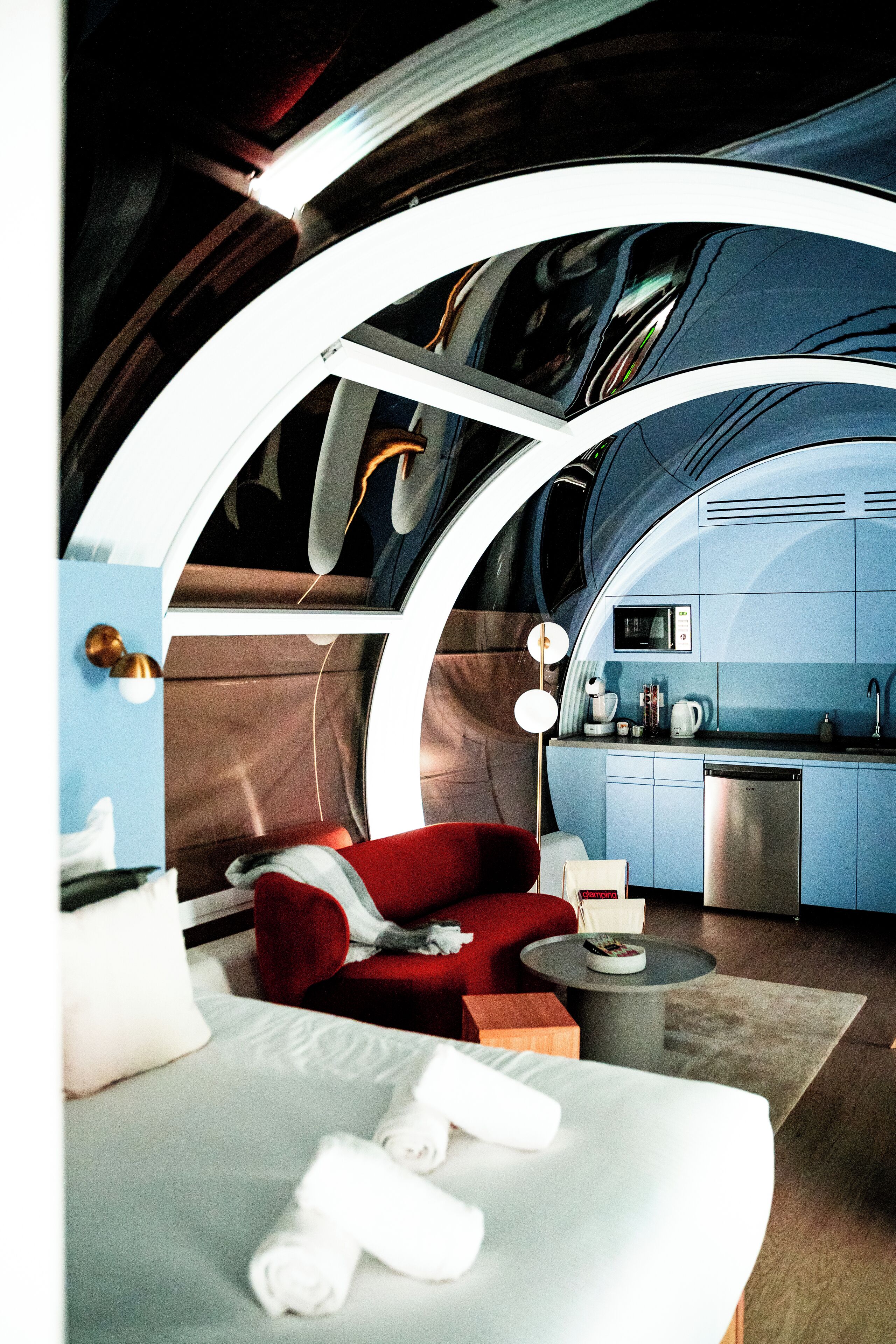 A modern interior with a bed, red sofa, and a kitchenette.