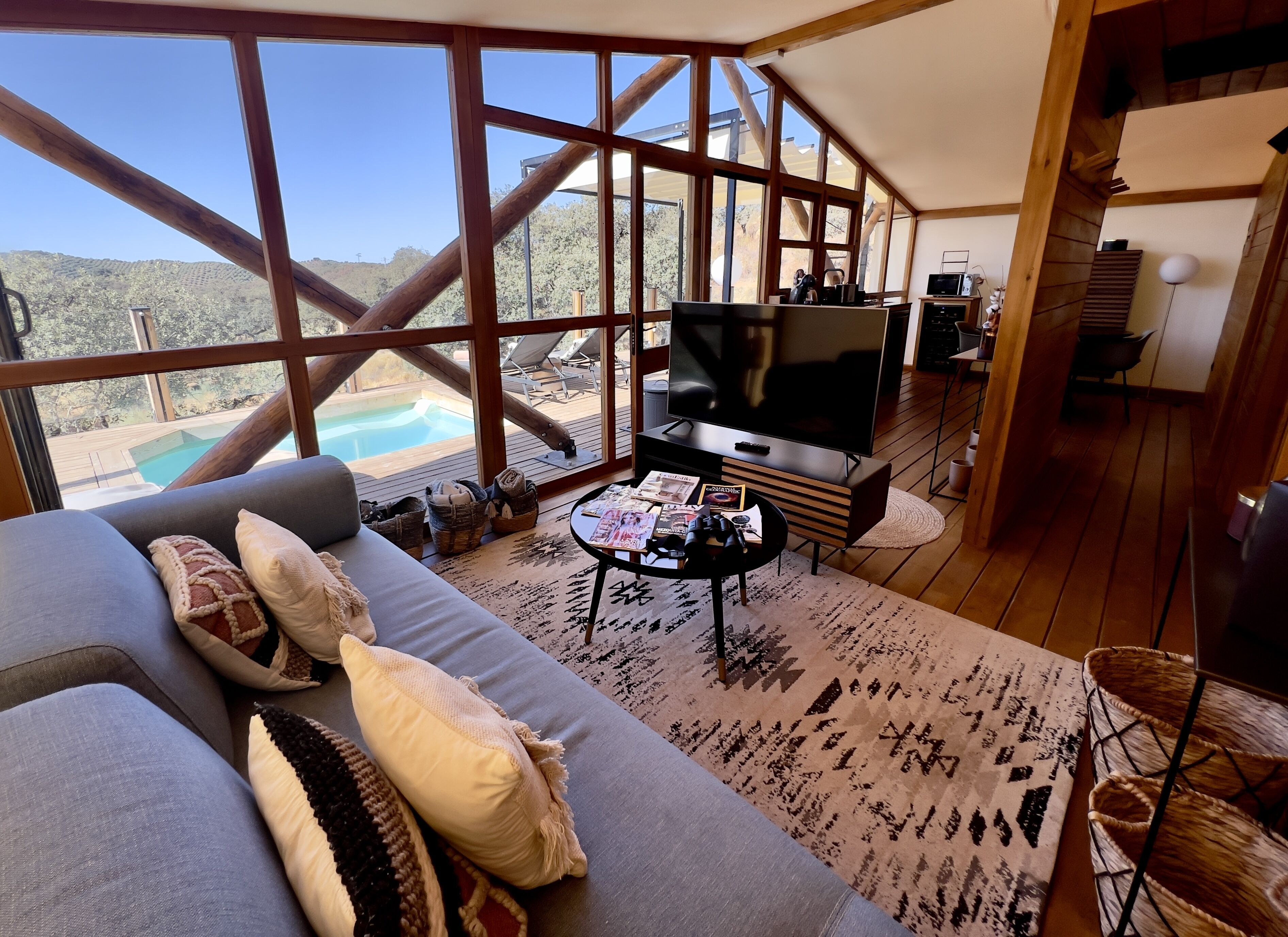 Un salon moderne doté d’un grand téléviseur, de sièges confortables et offrant une vue sur une piscine et des montagnes.