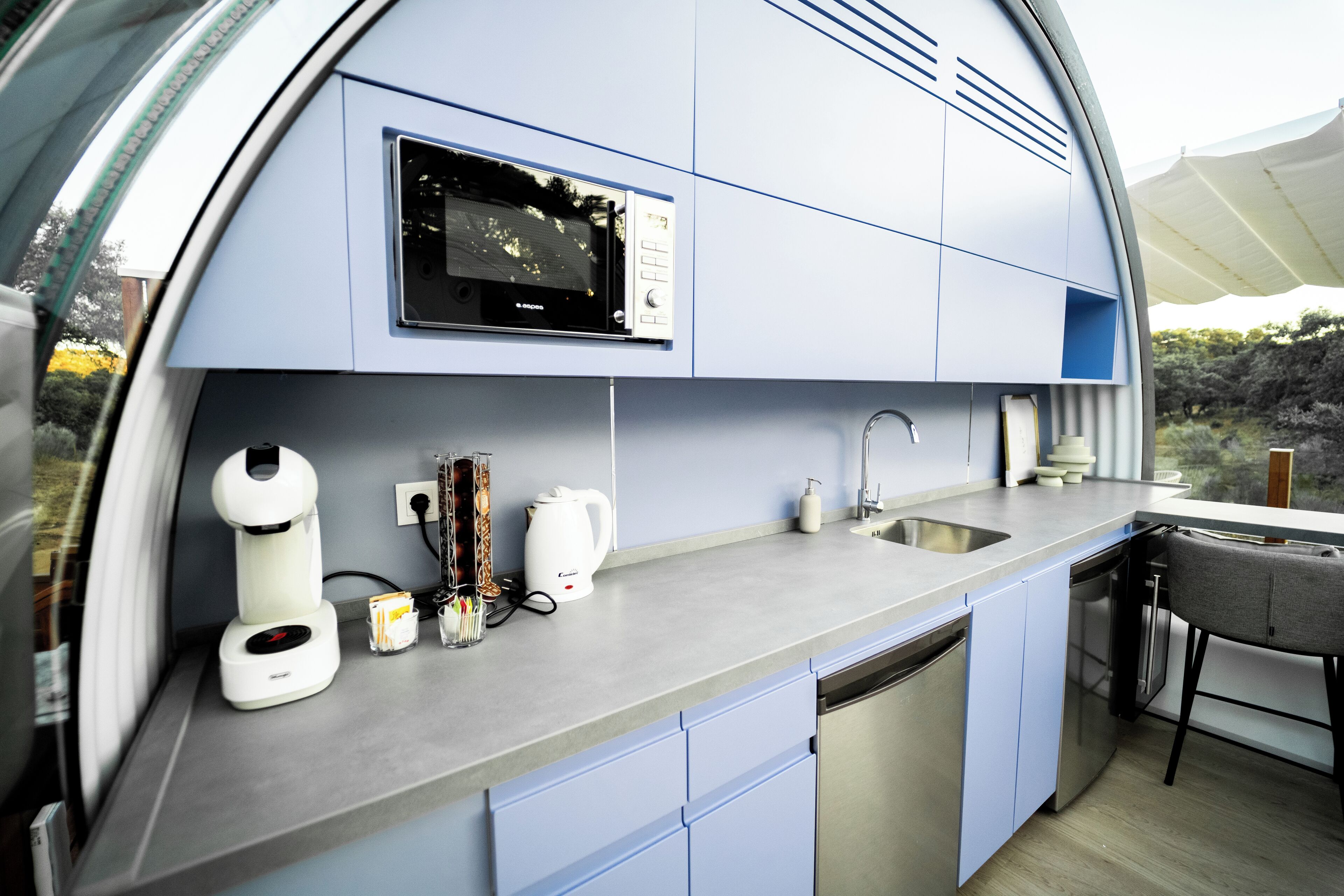 Una cocina compacta con microondas, cafetera y lavamanos.