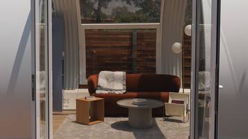 A modern, open-plan living space with a wooden deck, a sofa, a coffee table, and a glass door leading to an outdoor area.