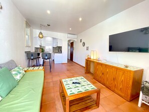Ein gemütlicher Wohnbereich mit einer Couch, einem Couchtisch, einem Fernseher, einer Holzkabine und einer Küchenzeile.