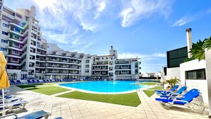 A swimming pool with blue lounge chairs and a grassy area, surrounded by multi-story buildings with balconies. - ALBUFEIRA SKYLIGHT 1 WITH POOL by HOMING (Albufeira)