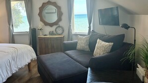 Une chambre avec un lit, un canapé, une petite table avec une horloge, un miroir, une télévision et une vue sur la mer.