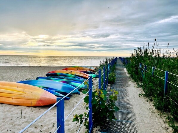 Una playa con una fila de kayaks de colores en la arena, un pasillo de metal y una valla.