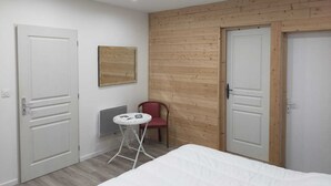 Een slaapkamer met een bed, twee witte deuren, een radiator, een klein rond tafeltje en een stoel.