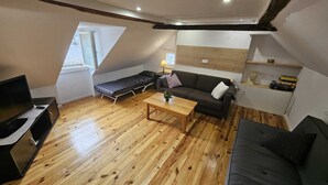 Een loft-achtige kamer met een houten vloer, een bank, een eettafel, een bed, een televisie en een raam.