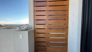 Puerta corredera de madera con listones horizontales, una piedra en el alféizar y vista al litoral.