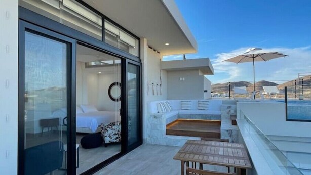 Un espacio exterior moderno con puerta de vidrio que da a un dormitorio, una mesa de madera y un sofá blanco.