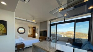 Una habitación de hotel moderna con cama, un pequeño rincón de descanso, un balcón con vistas y una kitchenette.