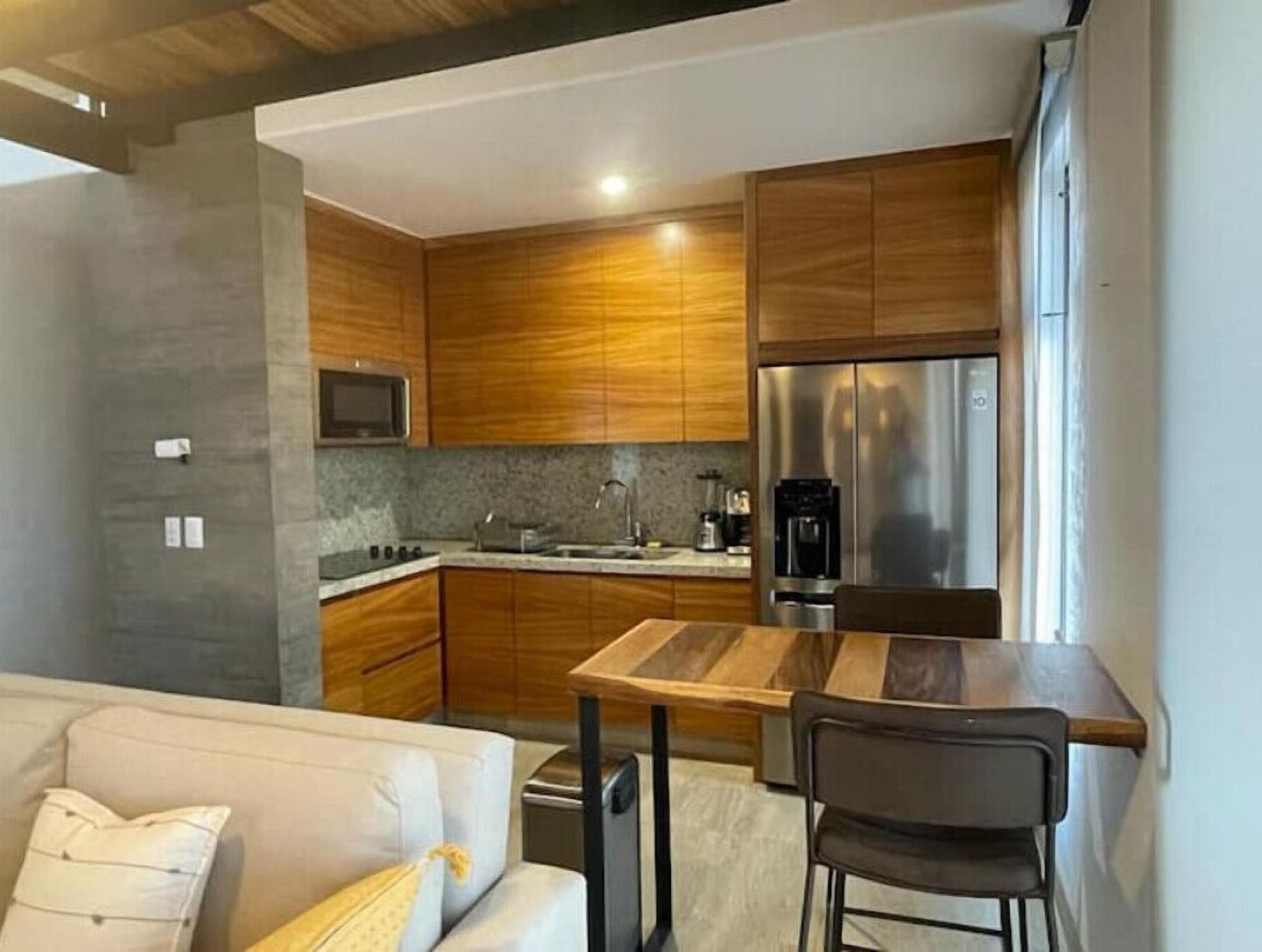 A modern kitchen with wooden cabinets, a stainless steel refrigerator, and a built-in microwave.