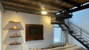 Een moderne woonkamer met een bank, een aan de muur bevestigde televisie, houten planken en een trap.