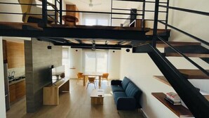 A modern loft-style apartment with a mezzanine, open-plan living area, kitchen, and dining space.
