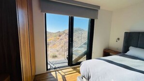 A bedroom with a large sliding glass door leading to a balcony with a view of a bridge and hills.