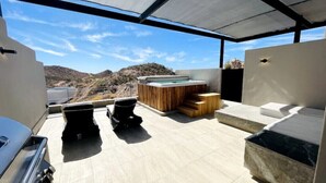 A rooftop terrace with a hot tub, seating area, and a view of the surrounding landscape.