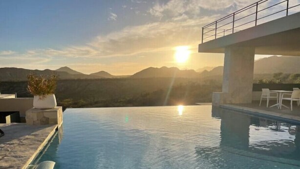 An infinity pool with a view of mountains and the sun setting in the background.