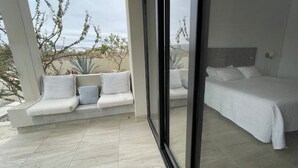 Une chambre moderne avec un grand lit, un coin salon avec des coussins et une vue sur l’extérieur.