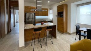 Une cuisine moderne dotée d’un îlot central, de tabourets de bar, d’un réfrigérateur en acier inoxydable et d’une fenêtre donnant sur un paysage urbain.