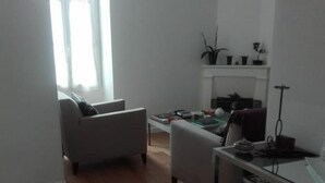 Un salon avec un canapé, une table basse et un meuble pour la télévision. Il y a une fenêtre avec des rideaux, une bibliothèque et une plante accrochée au mur.