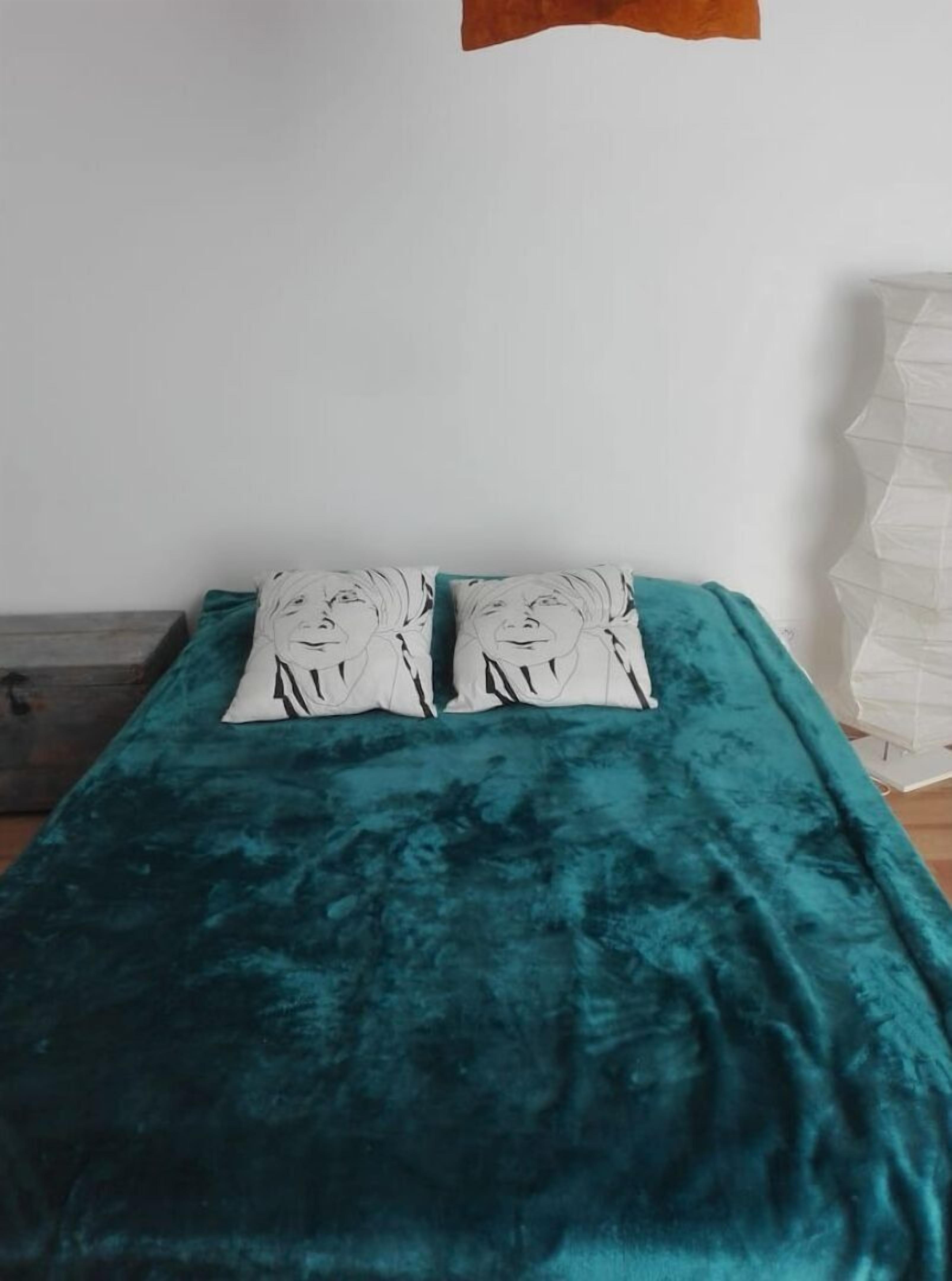 A bed with a teal bedspread and two pillows with a face design.