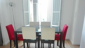 Un coin repas avec une table en verre et quatre chaises, un plancher en bois et une vue sur l’extérieur grâce à une grande fenêtre.