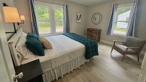 A bedroom with a bed, a chair, a nightstand, a dresser, and a window with curtains.