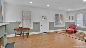 A spacious living room with hardwood flooring, a fireplace, a dining area with a wooden table and chairs, and a red leather armchair. - The Arrive on Rutherford (Shreveport)