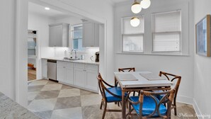 A modern kitchen with white cabinets, a dining table with blue chairs, and a chandelier. - The Arrive on Rutherford (Shreveport)
