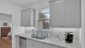 A kitchen with white cabinets, a double sink, and a coffee maker. - The Arrive on Rutherford (Shreveport)