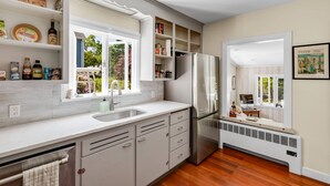 Une cuisine moderne avec des meubles blancs, un réfrigérateur en acier inoxydable et une fenêtre donnant sur un paysage verdoyant.