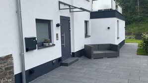 A modern two-story house with a flat roof, a balcony, and a paved driveway.