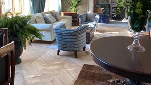 Un salon spacieux doté d’un parquet en point de Hongrie, d’un grand lustre et d’une cheminée.
