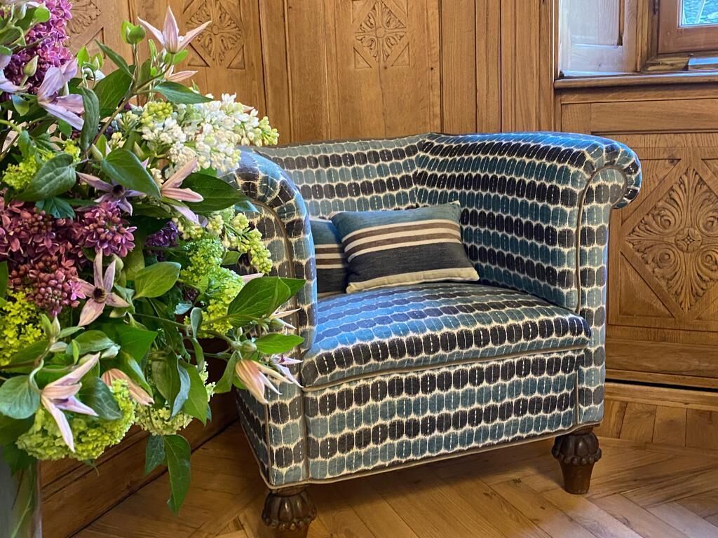 Ein gemustertes Sessel mit Kissen, neben einem großen Blumenarrangement platziert.