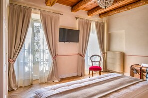 A bedroom with a wooden ceiling, a bed with a white duvet, a red chair, a radiator, and a television on the wall. - VILLA CHIOVENDA Residenza d'Epoca (Premosello Chiovenda)