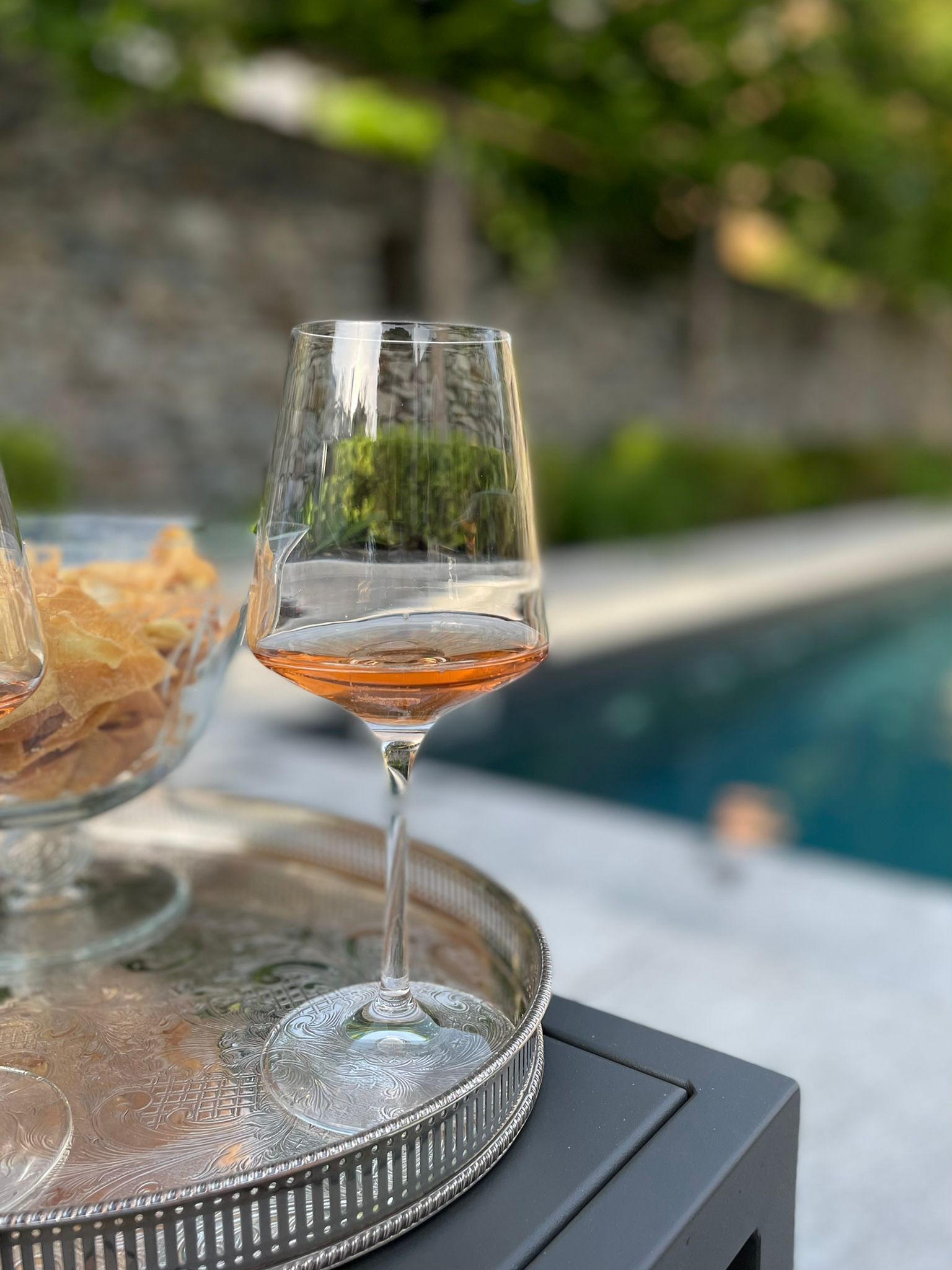 Ein Glas bernsteinfarbige Flüssigkeit auf einem Tablett mit silbernem Deckel, platziert auf einem Tisch in der Nähe eines Pools.